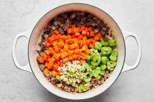 ground beef, chopped onion, carrots and celery and minced garlic being cooked in a large pot with olive oil.