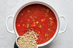 green lentils being added to a pot with spices, crushed tomatoes, broth, ground beef and veggies