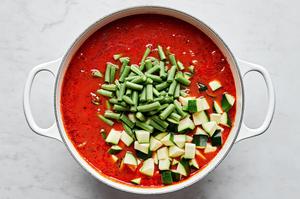 zucchini and green beans being added to a pot of beef and lentil soup