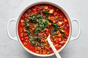 parsley and basil being stirred into a pot of beef and lentil soup