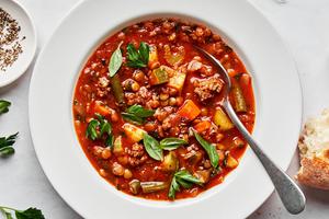 a bowl of homemade beef and lentil soup sprinkled with pepper, basil and parsley served with crusty bread