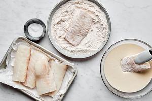 cod being dipped into a flour mixture then in a beer batter