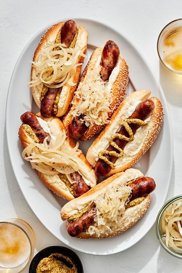 a platter of beer brats served on hoagie rolls topped with sauerkraut, onions, mustard and mayo