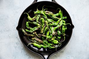 Blistered Shishito Peppers in olive oil in a black skillet