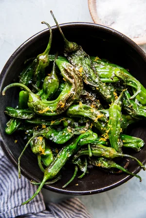 Blistered Shishito Peppers in olive oil, sea salt and lemon zest in a black bowl