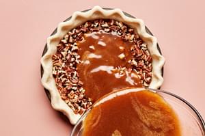 pie filling being poured on top of pecans layering the bottom of a pie crust