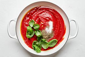 garlic, olive oil, tomatoes, salt, Italian seasoning, and basil leaves being cooked in a pot