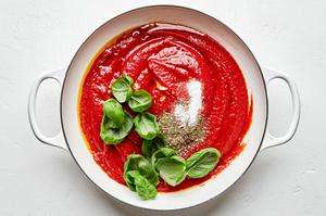 garlic, olive oil, tomatoes, salt, Italian seasoning, and basil leaves being cooked in a pot