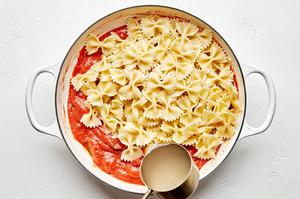 bow tie pasta being tossed in sauce made with tomatoes, basil, cream, spinach, sun dried tomatoes and topped with parmesan