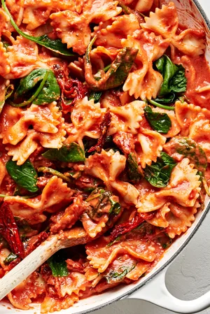 a pot of bow tie pasta made with tomatoes, basil, cream, spinach, sun dried tomatoes and topped with parmesan