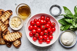 olive oil, cherry tomatoes, salt, basil, garlic, burrata and grilled bread slices in prep bowls to make braised tomatoes