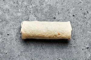 a breakfast burrito on the counter filled with sausage, eggs, potatoes, cilantro, avocado and salsa