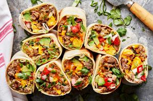 breakfast burritos sliced in half filled with potatoes, eggs, sausage, green onions, cheddar, avocado, salsa and cilantro
