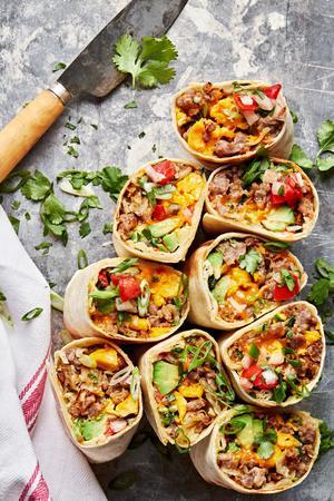 breakfast burritos sliced in half filled with potatoes, eggs, sausage, green onions, cheddar, avocado, salsa and cilantro