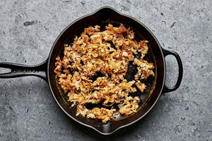 shredded potatoes being cooked in a skillet with olive oil and salt