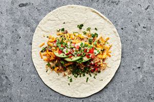 a flour tortilla being filled with sausage, eggs, potatoes, cilantro, avocado and salsa