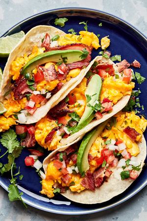 breakfast tacos made with eggs, bacon, cilantro, sliced avocado, pico de gallo, and a squeeze of lime juice & hot sauce