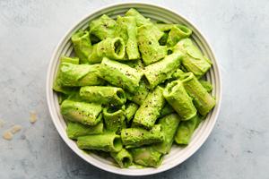 broccoli pesto pasta with rigatoni, garlic parmesan, olive oil, pine nuts, salt, basil in a bowl