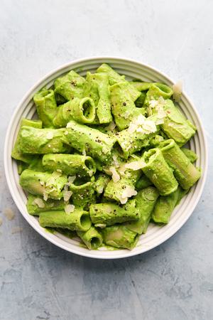 Rigatoni pasta with broccoli pesto in a bowl with a spoon with parmesan and one nuts