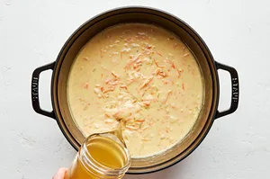 chicken stock, onion, carrot, garlic, butter, flour, spices and milk cooking in a pot to make cozy broccoli cheddar soup