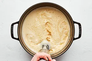 broccoli cheddar soup being blended with an immersion blender in a soup pot