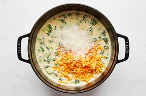 parmesan and cheddar being added to a pot of homemade broccoli cheddar soup