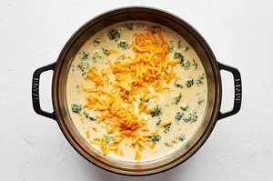 parmesan and cheddar being added to a pot of broccoli cheddar soup, a cozy fall and winter dinner