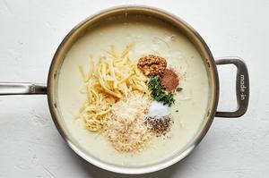 mustard, spices, and cheese being added to a pan with shallots, flour, butter and milk making sauce for au gratin