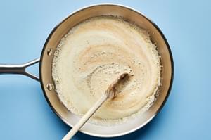 butter being browned in a skillet and stirred with a wooden spoon
