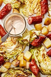roasted cabbage, sausage and potatoes on a rimmed baking sheet wit a jar of homemade sour cream sauce for serving