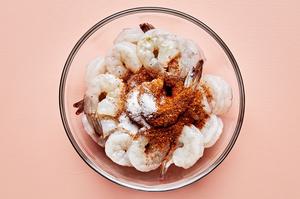 raw shrimp being tossed with olive oil, lemon juice, cajun seasoning & salt in a glass bowl