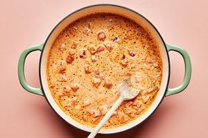 cajun pasta sauce in a large pot being stirred with a wooden spoon