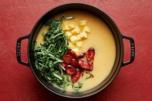 collard greens, potatoes and smoked sausage being added back into a soup pot with blended soup