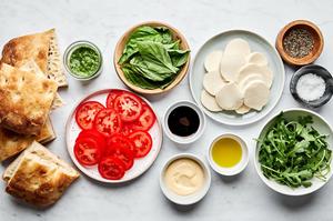 focaccia, pesto, tomatoes, mozzarella, mayo, balsamic, arugula and basil in prep bowls to make a caprese sandwich