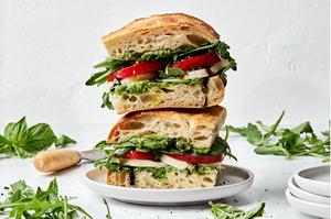 2 caprese sandwiches stacked on top of each other made with focaccia, pesto, mozzarella, tomato, arugula, and balsamic glaze