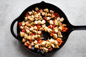 chicken marinated in cornstarch, salt and soy sauce, being cooked in a large black skillet with bell pepper