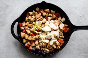 chicken being cooked in a large black skillet with red bell pepper, ginger, garlic and water chestnuts.