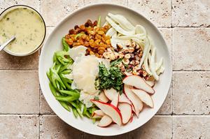 celery, fennel bulb, pears, hazelnuts, parmesan, raisins, and tarragon being tossed in a bowl