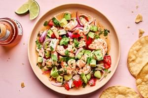 a bowl of ceviche made with shrimp, avocado, tomato, cucumber, red onion and cilantro served with tortilla chips and a beer