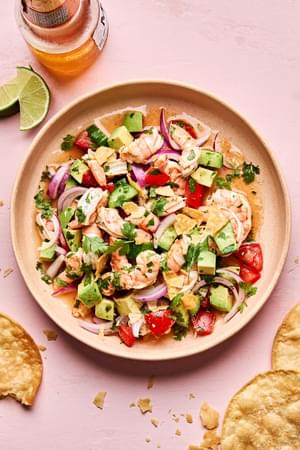 a bowl of ceviche made with shrimp, avocado, tomato, cucumber,  red onion and cilantro served with tortilla chips and a beer
