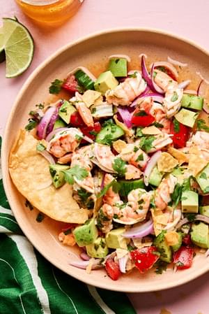 a bowl of ceviche made with shrimp, avocado, tomato, cucumber, red onion and cilantro served with tortilla chips and a beer