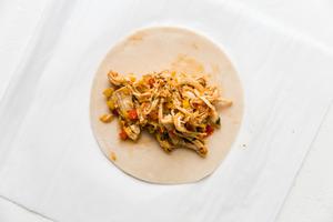 a empanada dough round topped with cooked chicken filling on parchment paper