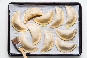 10 uncooked chicken empanadas on a parchment paper lined baking sheet.