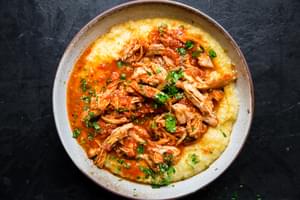 shredded chicken thighs in marinara sauce over creamy polenta in a bowl