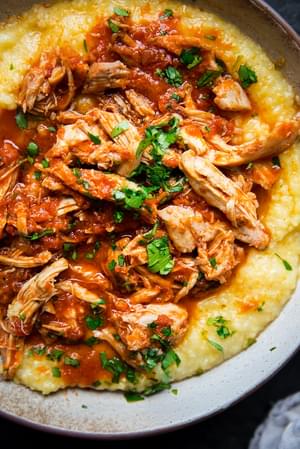 shredded chicken thighs in marinara sauce over creamy polenta in a bowl