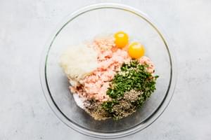 ground chicken, eggs, onions and parsley in a glass bowl to make chicken meatballs