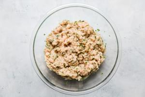 ground chicken, eggs, onions and parsley mixed together in a glass bowl to make chicken meatballs