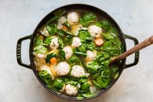 chicken meatball soup being stirred in a pot made with onion, garlic, chicken stock, fennel seeds, salt, carrots & potatoes