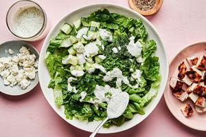 lettuce and fresh herbs being drizzled with chèvre ranch next to a bowl of grilled chicken