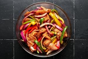 chicken, peppers and onions being tossed with homemade taco seasoning in a bowl